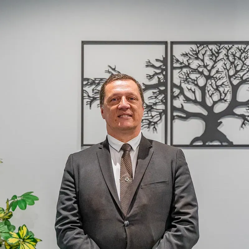 Portrait d'un conseiller funéraire en costume devant une décoration murale d'arbre.